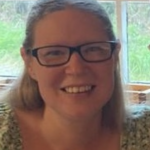 A headshot of a lady with long hair wearing glasses and smiling at the camera.